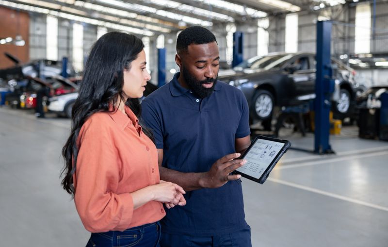 Mechanic working at an auto repair shop and showing a woman the diagnosis of her car using a tablet