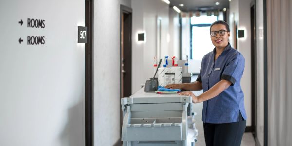 Hotel housekeeper with cleaning cart in hallway near room 507.