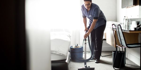 Hotel housekeeper vacuuming a carpeted room.
