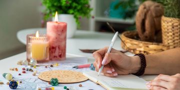 Person writing in a notebook with candles and crystals on the table.