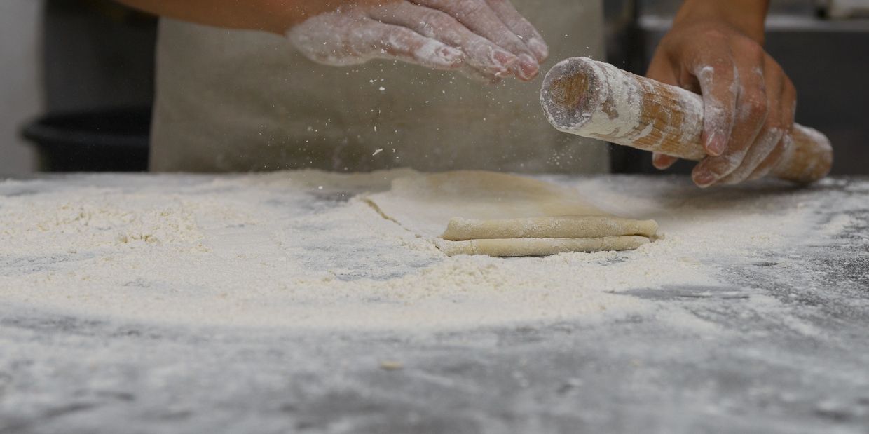 Hands dusted with flour rolling dough on a floured surface.