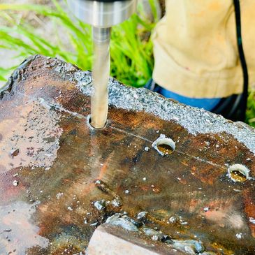 Close-up of a drill bit making holes in a rusty metal surface outdoors.