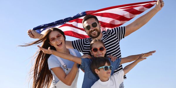 Family holding American flag, smiling and wearing sunglasses.