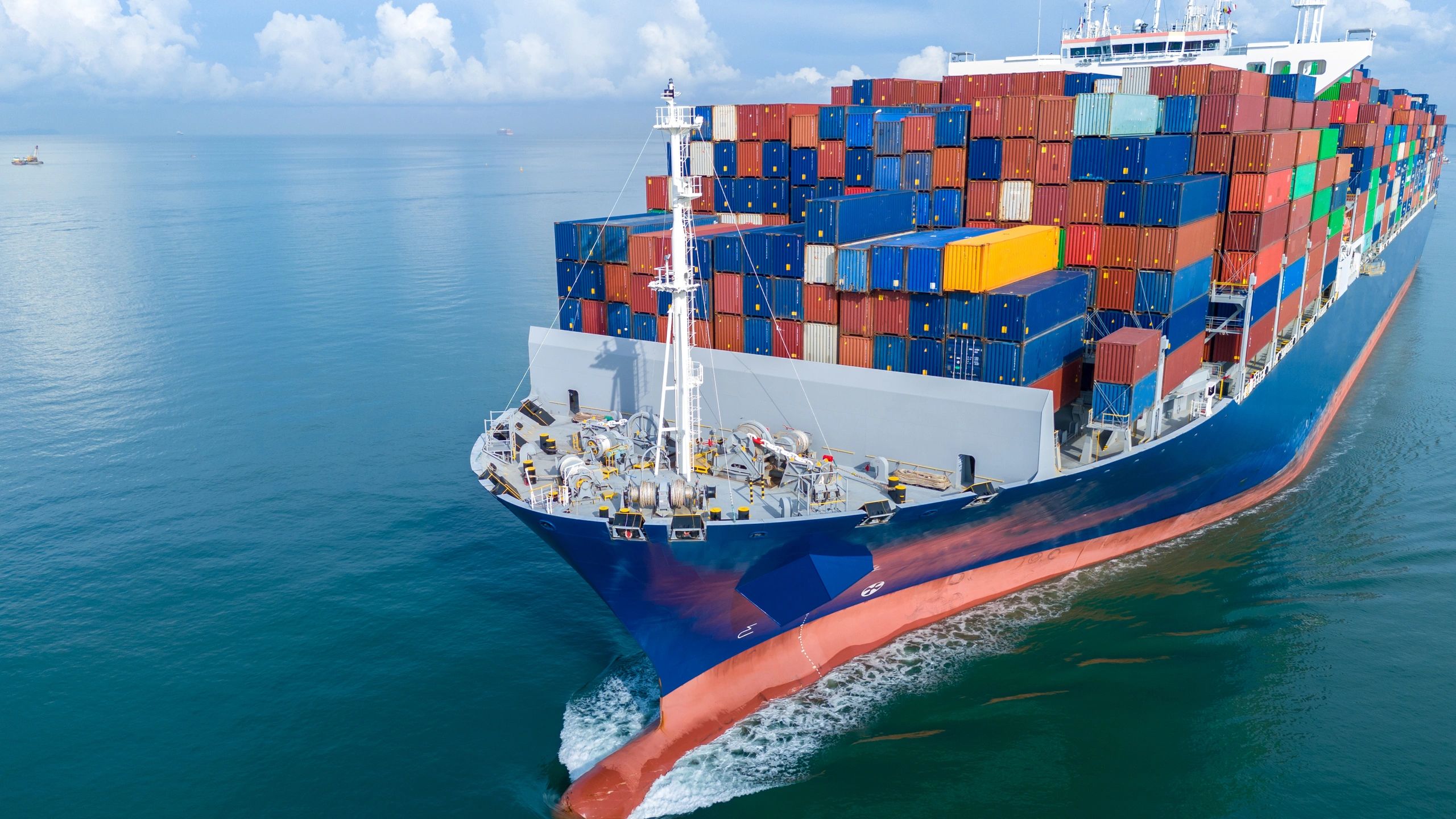 A large cargo ship loaded with colorful shipping containers sails through calm waters.