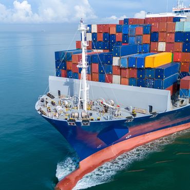 A large cargo ship loaded with colorful shipping containers sails through calm waters.