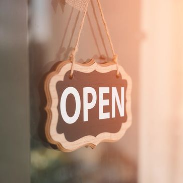 Wooden open sign hanging on a door with sunlight.