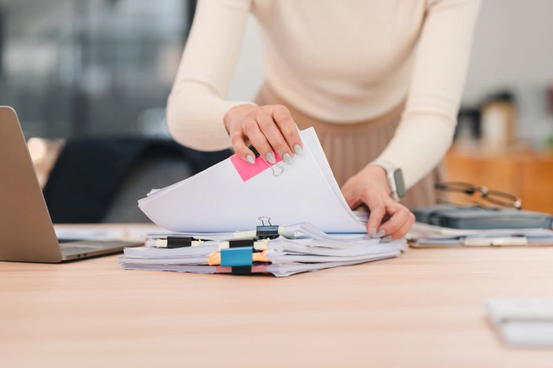 An Organized office worker sorting documents on desk with laptop