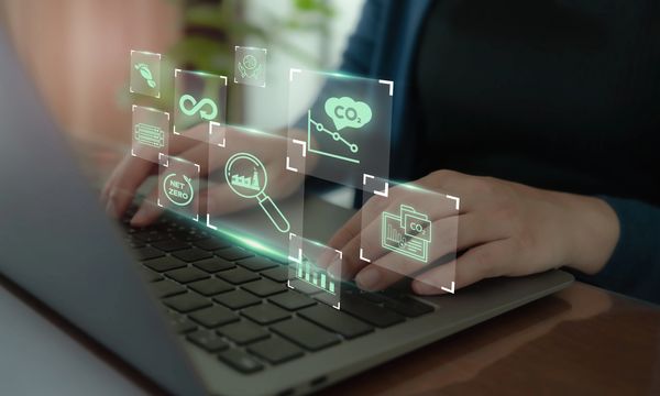 Person typing on laptop with floating carbon footprint and sustainability icons.