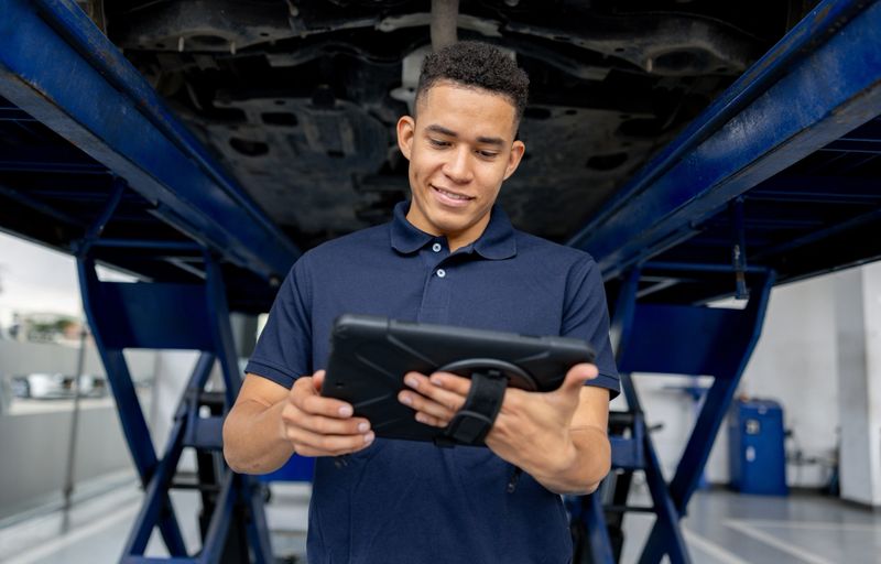 Latin American mechanic at a car garage using a digital tablet to look at a vehicleâs diagnosis while fixing it