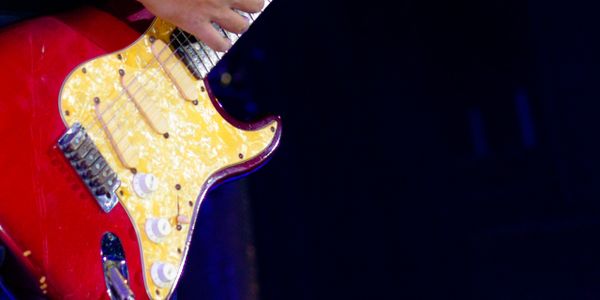 Close-up of a hand playing a red electric guitar on stage.