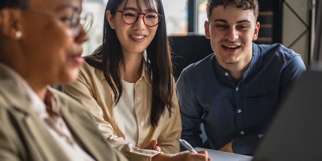 Three diverse colleagues collaborating happily around a laptop in a bright office.
