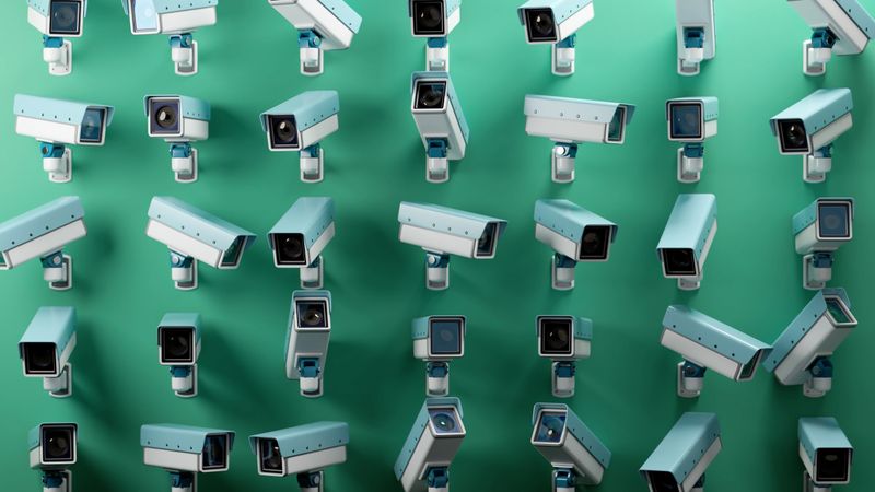 An array of multiple security cameras mounted on a green wall, symbolizing surveillance, security, and monitoring. The uniform arrangement emphasizes themes of protection, technolog, and observation.