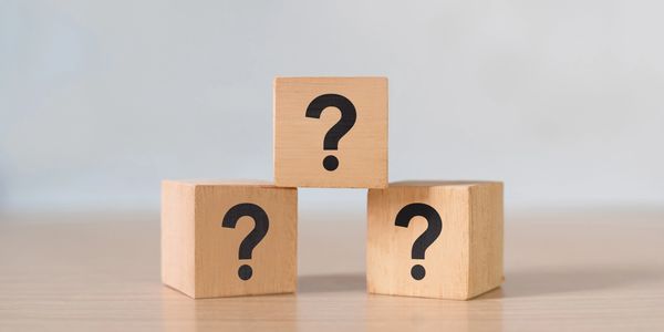 Three wooden blocks with question marks stacked in a pyramid shape.