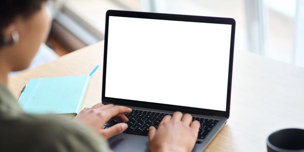 Person typing on a laptop with a blank white screen at a desk.