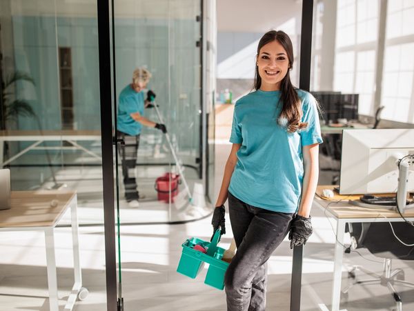 Smiling cleaner holding mop bucket.