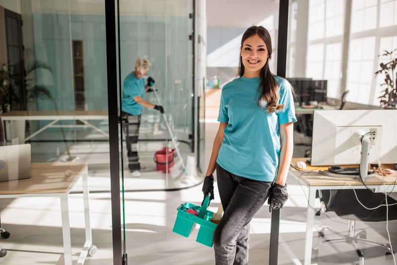 Young woman from a professional cleaning team standing proudly in a sleek, contemporary office space
