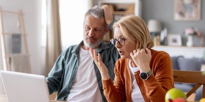 Senior couple looking confused while using a laptop in their kitchen.