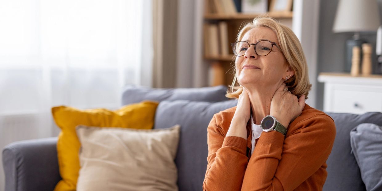 Middle-aged woman massaging her neck while sitting on a couch.