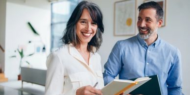Two coworkers smiling with notebooks in an office.