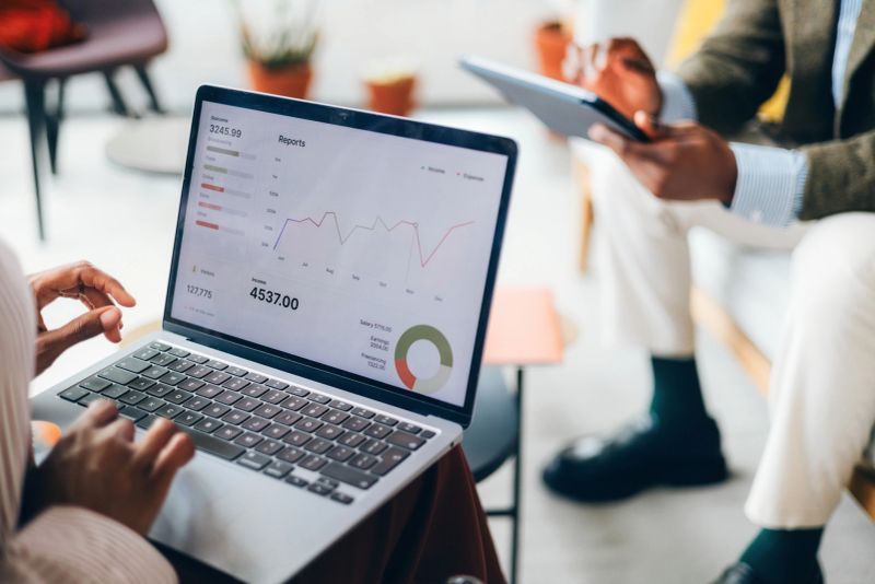 Colleagues review important financial data presented on a laptop screen, sharing insights and strategies. The image conveys both collaboration and a professional workplace environment, emphasizing analysis and teamwork.