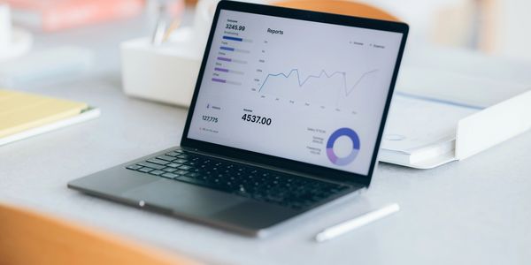 Laptop displaying financial reports and graphs on a desk.