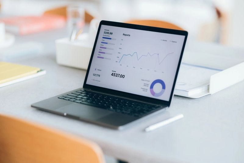 A workspace featuring a laptop showing financial graphs and analytical charts, sitting on a modern desktop. The setting emphasizes productivity, data-driven decisions, and a contemporary approach to office organization.