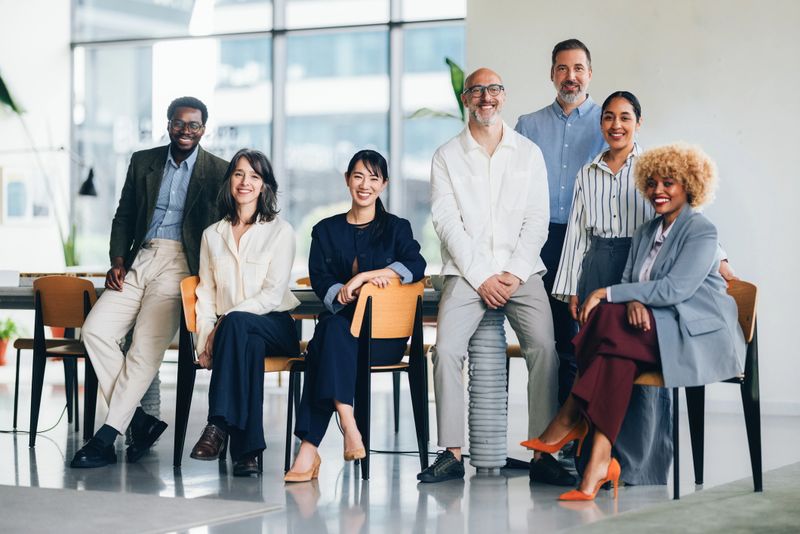 A group of professionals form a diverse team working together in a modern office. They are interacting and smiling, emphasizing collaboration, diversity, and teamwork in a corporate setting.