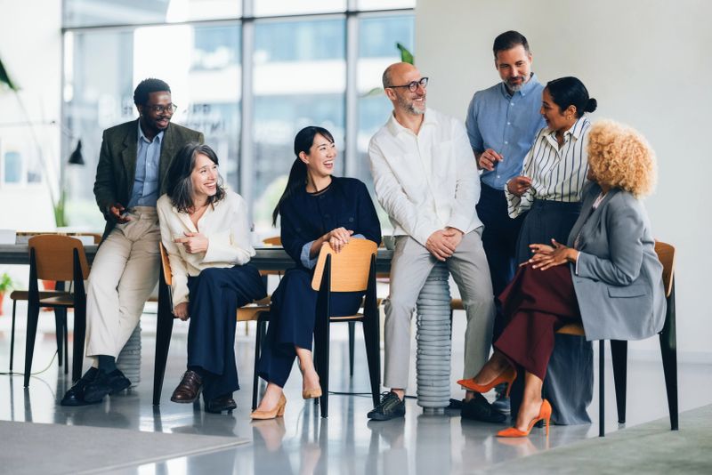 A group of professional colleagues engaging in a lighthearted conversation, showcasing diversity, teamwork, and camaraderie in a corporate environment, emphasizing human connection and workplace inclusion.