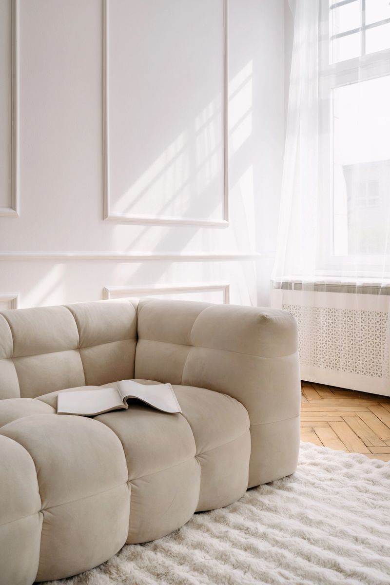 Airy living space with a comfortable white couch, a open book and sunlight streaming through the large windows, creating a serene atmosphere at home with morning light in room, vertical shot