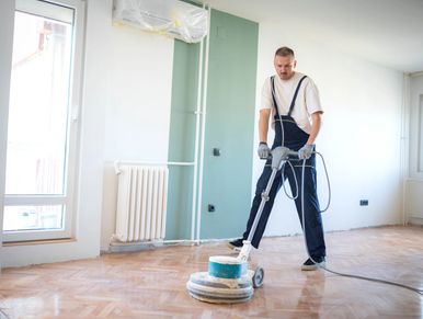 Man using a floor polishing machine on wooden floor.