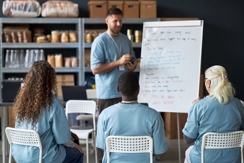 Group seated in classroom setting with instructor teaching business strategies using whiteboard. Attendees paying attention, various demographics and age groups represented