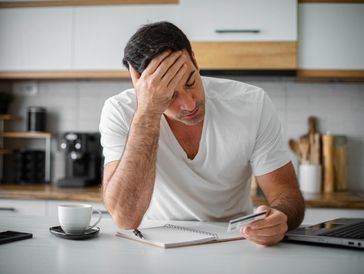 Man looks stressed while reviewing bills in kitchen.