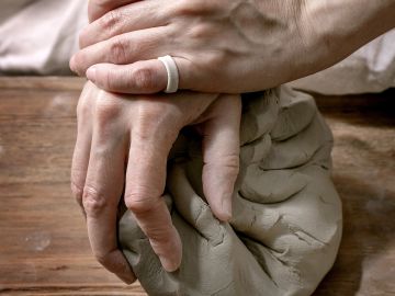 Hands kneading clay on a wooden surface.