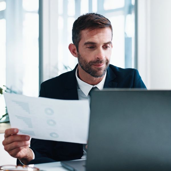 Business consultant analyzing financial reports on laptop.