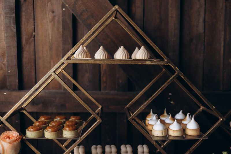 Beautiful arrangement of gourmet desserts displayed on a geometric metal shelf in a rustic setting. Warm lighting enhances the elegant presentation, highlighting a sophisticated and inviting culinary experience.