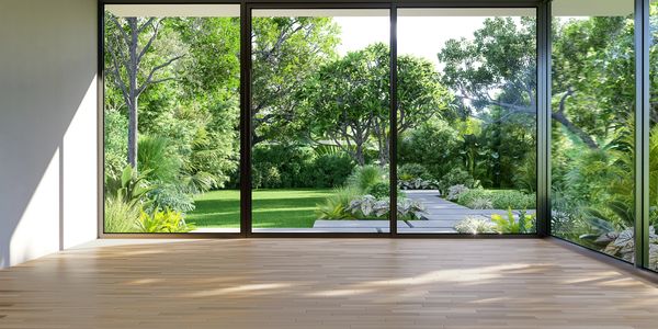 Empty room with large glass windows overlooking a lush garden.