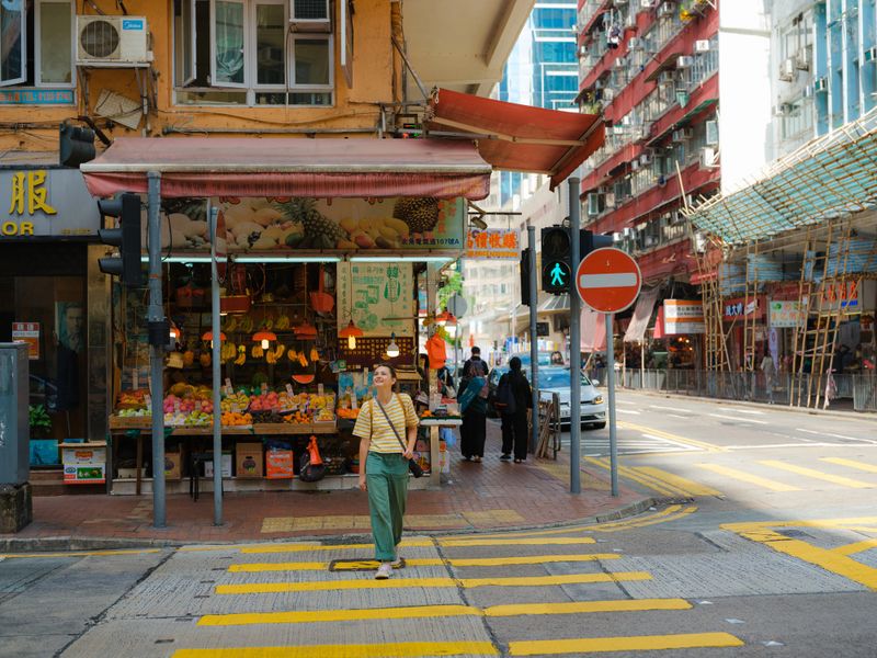 Woman walks through a bustling Hong Kong street, surrounded by colorful signs and high-rise buildings. She pauses to take in the energy of the city during her daytime exploration.