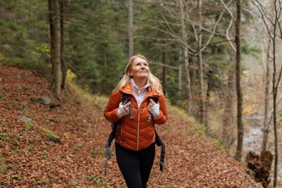 A woman hiking on a forest trail in autumn, looking up and smiling.