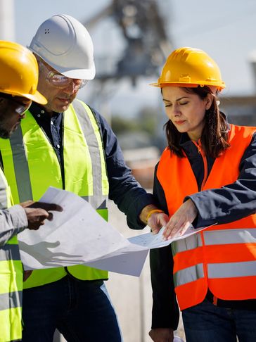 Three construction workers reviewing blueprints on site wearing safety gear.