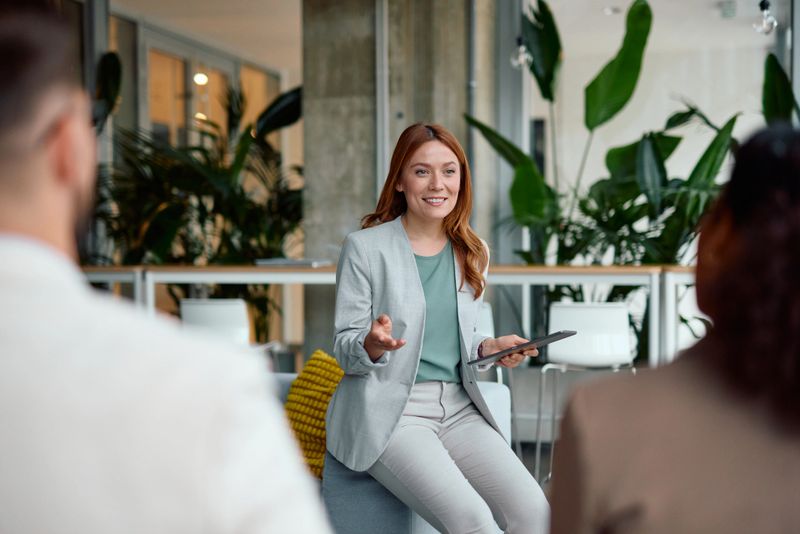 Young businesswoman is holding a tablet and leading a meeting with her team, discussing new strategies and projects in a modern office environment