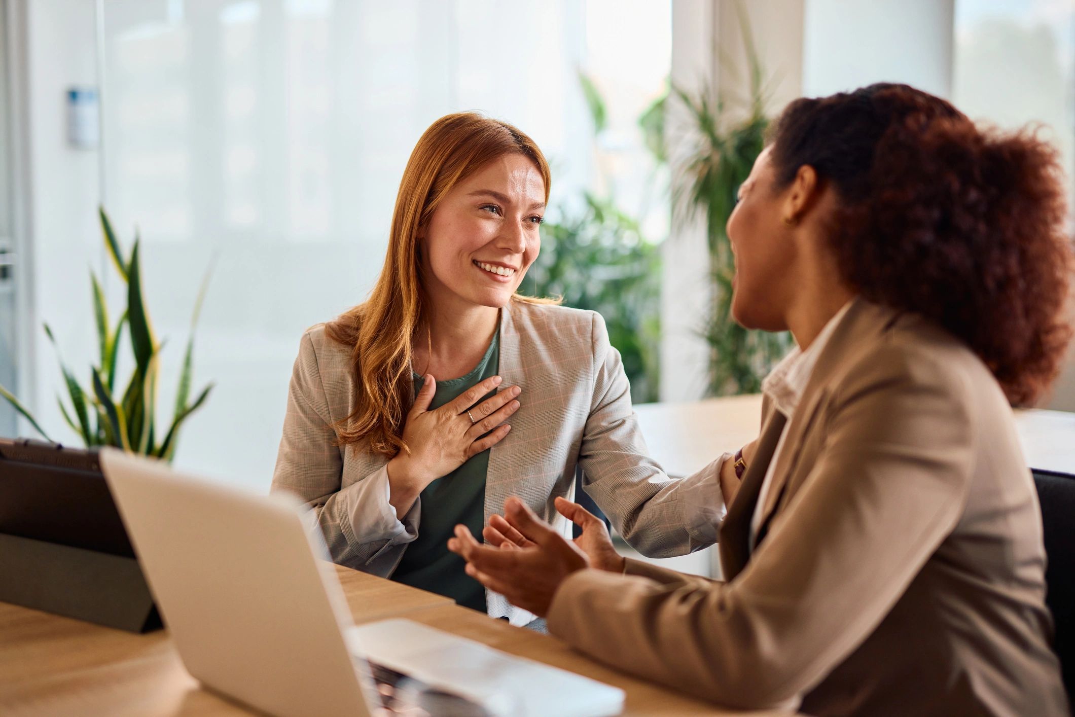 Two women engage in a warm, supportive conversation in a bright office setting.