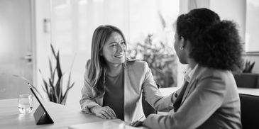 Two people sit at a desk, smiling and talking in a warm, professional support meeting.