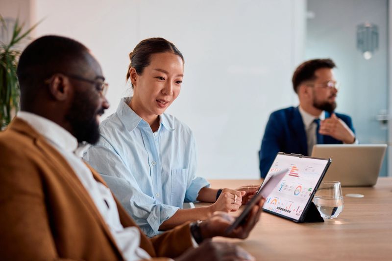 Two business colleagues collaborating in an office, using a digital tablet to analyze financial data and statistics displayed on the screen during their meeting