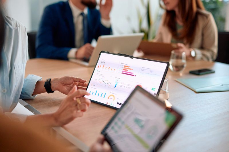 Business colleagues are discussing company performance, pointing at charts and graphs displayed on a tablet during a productive meeting in the office