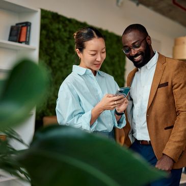 Two colleagues smiling while looking at a phone.