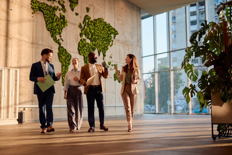 Four businesspeople walking and talking in a modern office with a lush moss wall, discussing innovative ideas and projects while radiating teamwork and collaboration