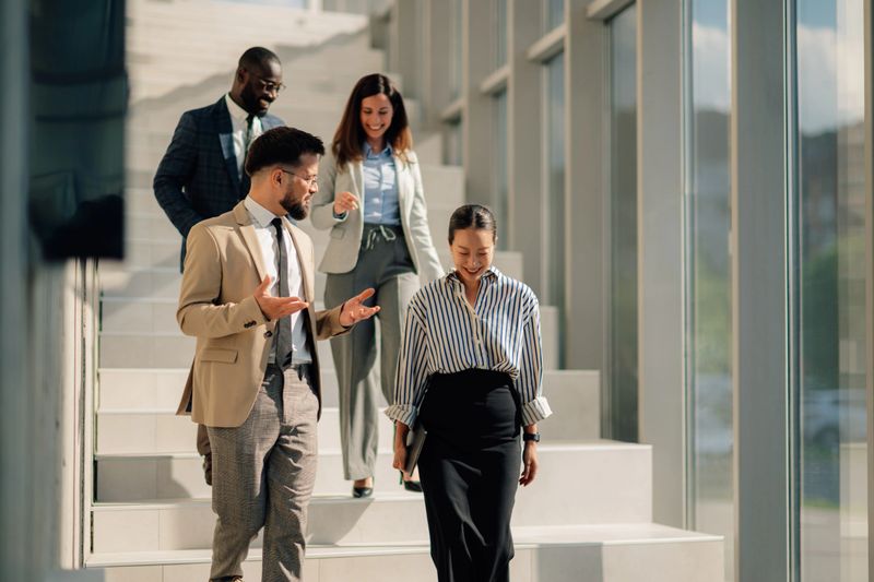 Multi-ethnic business team descending stairs, discussing work in a bright, modern office space