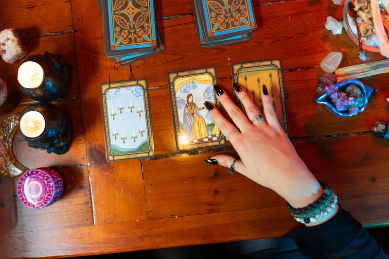 Fortune teller interpreting tarot cards spread on a wooden table, surrounded by mystical objects and lit by candles, creating a mysterious atmosphere