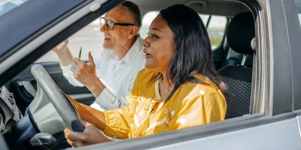 Driving instructor guiding a woman in a car.