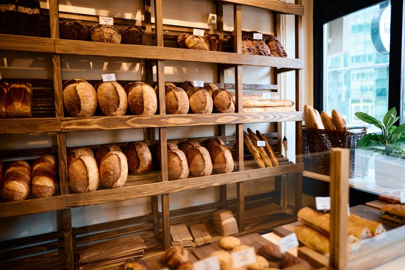 Freshly baked loaves of bread are neatly arranged on rustic wooden shelves in a bakery shop, creating a warm and inviting atmosphere for customers